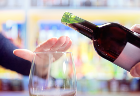 Womans hand rejecting more alcohol from wine bottle in bar